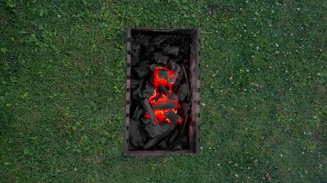 Top view of a metal grill with glowing red charcoal embers burning on a green grass lawn
