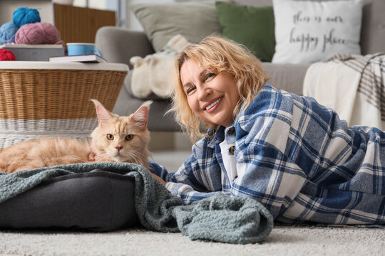 Beautiful middle-aged woman lying near cute cat in pet bed at home