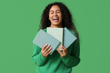 Fototapeta premium Happy young African-American woman with books on green background