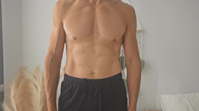 Shirtless hispanic man showing bare chest and abdomen standing with arms at sides in a studio; vulnerability health.