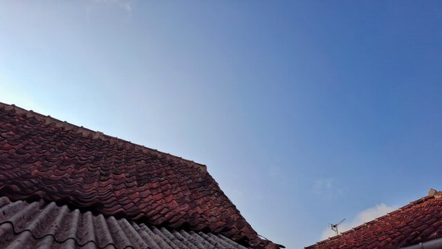 Traditional clay tile rooftops viewed from below against a clear blue sky, featuring rustic roofing textures and residential architecture.