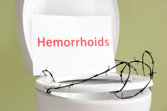 Toilet bowl with word HEMORRHOIDS and barbed wire on green background, closeup