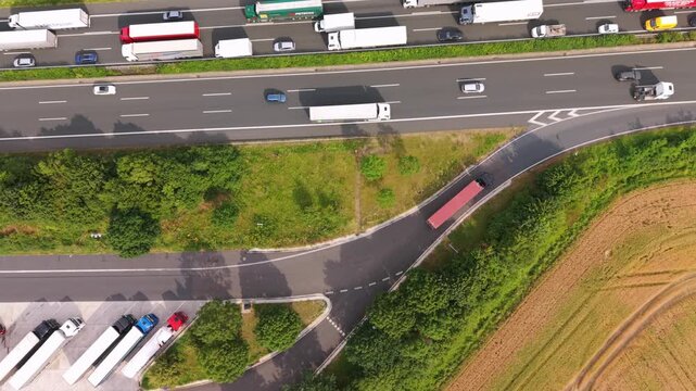 Aerial perspective of a bustling highway with trucks and cars, highlighting a truck making a turn onto a side road amidst greenery and fields