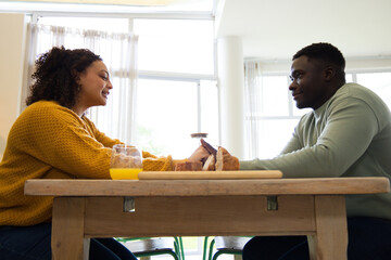 Fototapeta premium African American couple sitting at table holding hands in mustard sweater and green top with bread