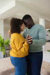 Obraz premium African American couple holding hands swaying at home near sofa wearing mustard knit and green top