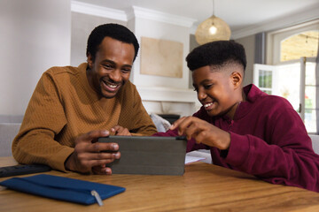 Obraz premium African American father and teenage son leaning and tapping tablet in living room with papers