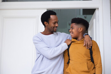 Naklejka premium African American father and teenage son standing at entry, smiling, wearing sweater hoodie backpack