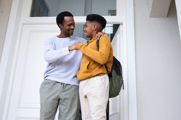 Naklejka premium African American father with teen son sharing fist bump at doorway, backpack visible, white door