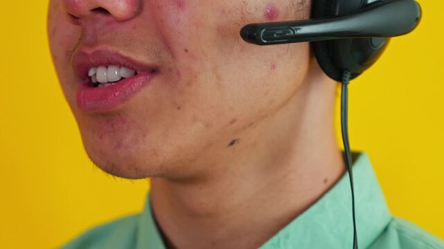 Close-up of male call center operator adjusting microphone and talking isolated on yellow backdrop