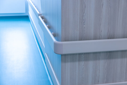 A rounded corner guard meets the handrail on a wall panel of a hospital corridor. Patients lean on such rails while walking during rehabilitation. Close up of an accessible new hospital