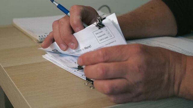 Business Worker Sorting Paper Documents.Close up of office worker hands sorting paper documents with a pen and binder clips, illustrating business administration, accounting, finance, paperwork,