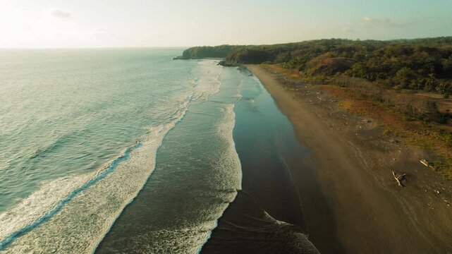 Aerial view of sand beach coastline with calm ocean waves at golden sunset light
