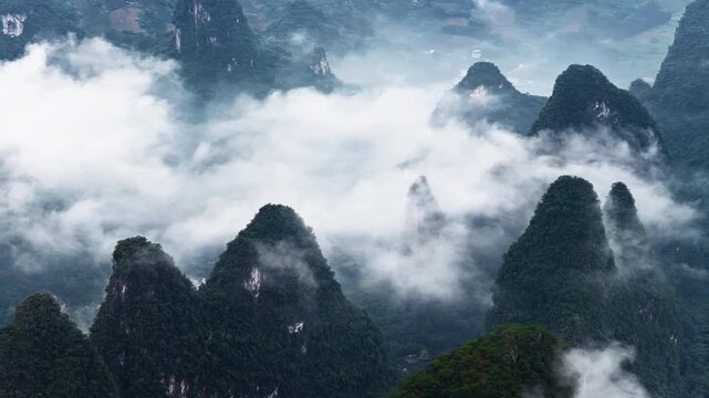 High angle view of limestone karst mountains surrounded by thick white fog and clouds under soft morning light in Guilin, China.