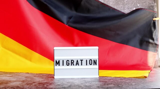 Lightbox with text MIGRATION flow. National symbol of Germany. German wave silky flag background. Concept of human migration crisis and population refugee movement. Demographic change 