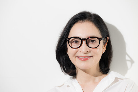 [白背景]眼鏡をかけた50代女性のポートレート、知的で落ち着いた印象のミドル世代とアイウェアのイメージ クローズアップ 　カメラ目線