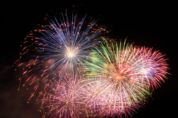 Obraz premium Bright and colorful pyrotechnic bursts illuminate the deep night sky, casting a radiant glow and festive energy during a spectacular outdoor celebration event