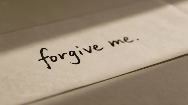 Minimalist overhead shot of a handwritten "forgive me" message on a clean paper surface, conveying deep emotion.