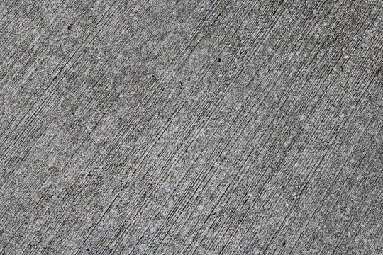 A full-frame minimalist background texture featuring grey broom-finished concrete with fine parallel lines running diagonally.