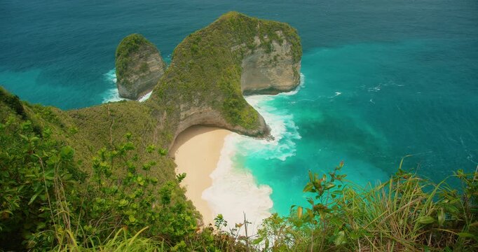 Trex shaped rock formation rises above white sand at Kelingking Beach Bali Nusa Penida