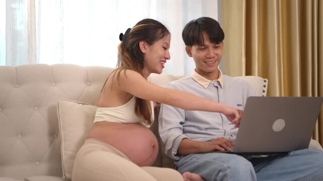 An expectant couple is relaxing at home, the man is using a laptop to look up information on prenatal and newborn care in preparation for their baby's imminent arrival