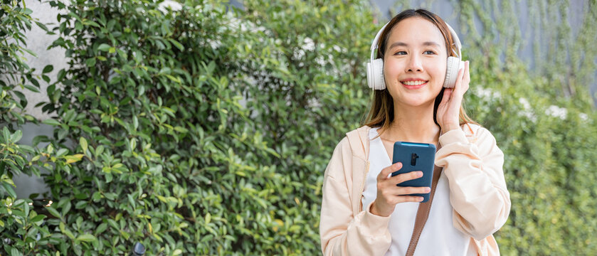 On beautiful spring day young woman with her bicycle is walking outdoors in park listening to music with earphones and typing joyful message on her mobile phone. Her happiness is infectious.