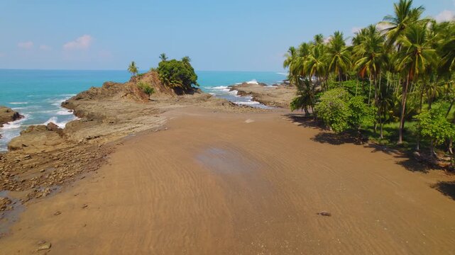 Sandy shore leads to rocky outcrop with Pacific ocean and palm trees in Costa Rica