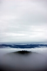 Fototapeta premium Misty Mountain Peak with Clouds and Forests in the Distance
