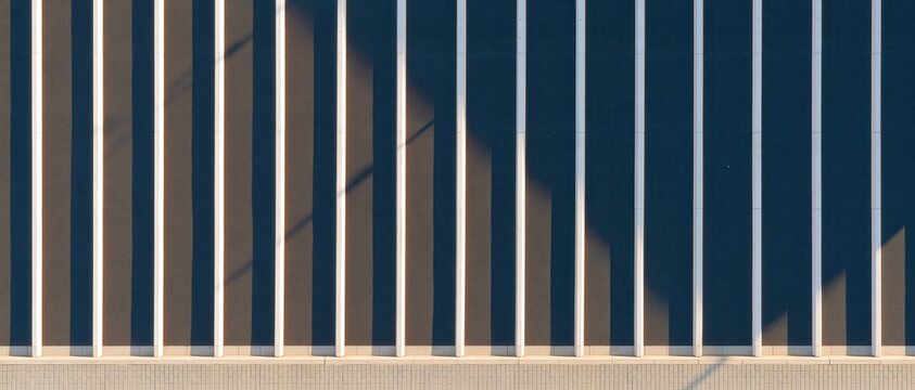Vertical white beams casting sharp shadows on dark wall, abstract architectural pattern