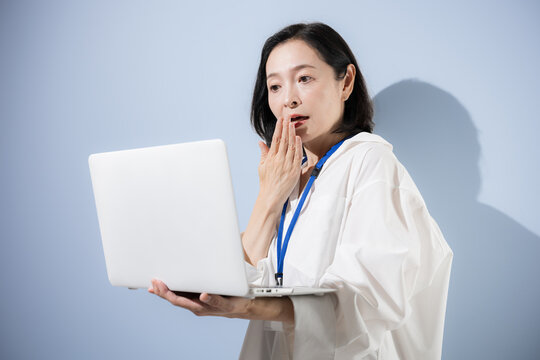 A close-up of a female office worker looking at her laptop with expressions of surprise, shock, and confusion&mdash;a Japanese businesswoman struggling with work-related issues, mistakes, problems, and stre