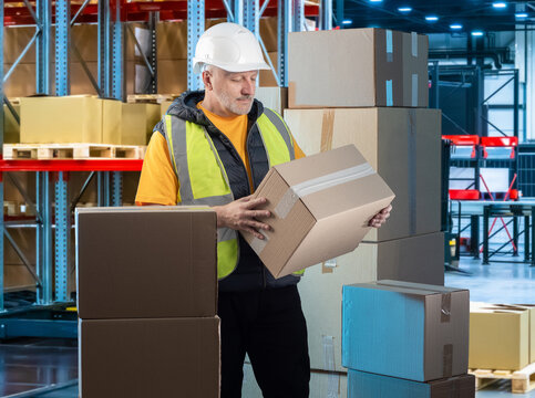 Warehouse logistics, worker handles cardboard boxes and prepares goods for storage, order fulfillment, packing and shipment in a distribution center.