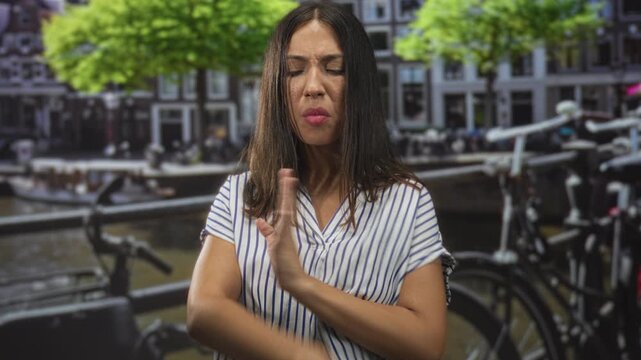 Woman pointing arm outward and sticking out tongue on street near canal railing and bicycles; playful defiance.