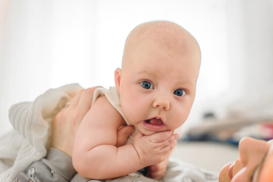 Baby 5-6 months old lies on mother's stomach while she supports the child with her hands and looks at the baby at home