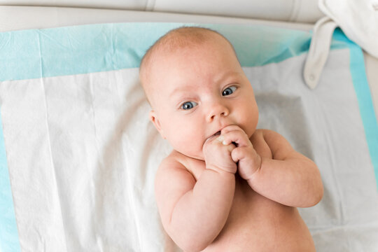 Baby 5-6 months old lies on back and sucks fingers during everyday care at home, natural self soothing behavior