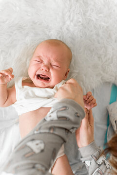Mother dresses baby 5-6 months old at home while the child cries during everyday care and changing clothes