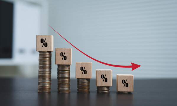 Financial concept of economic decline, falling interest rates, or shrinking profits represented by wooden block with percentage symbols on decreasing stacks of coins with downward red trend arrow.