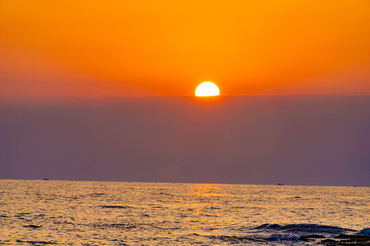 Brilliant orange sunset sinking into the sea beneath a thin cloud layer