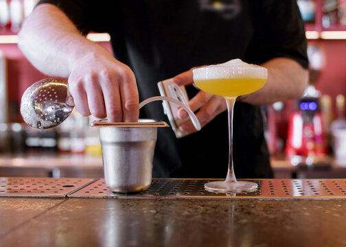 Foaming cocktail. Pub service. Bartender male hand making frothy top for drink glass with professional electronic device on counter.