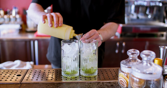 Cocktail recipe. Bartender service. Man hand measuring syrup pouring aroma liquid for to ice glass drink from squeezer to metal jigger.