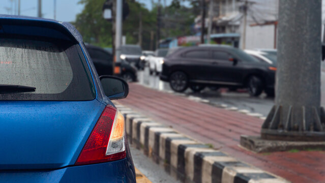 Rear view of a blue car with turn on right signal. Prepare for U-Turn. Several cars are making U-turns to the opposite side ahead. Beside a red tiled sidewalk along an urban street on an overcast day.