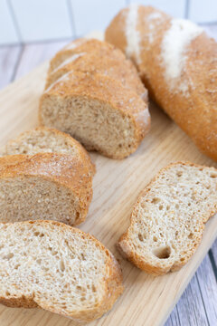 Freshly baked loaf rests on wooden board. Golden crust cradles soft, airy interior. Each slice reveals inviting, porous texture. Slices arranged for immediate serving.