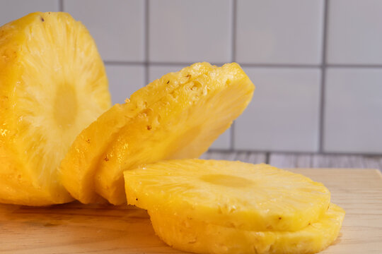 Freshly cut pineapple slices on wooden board. White tiled background adds clean, fresh vibe. Ideal for tropical food, healthy eating, or summer-themed content