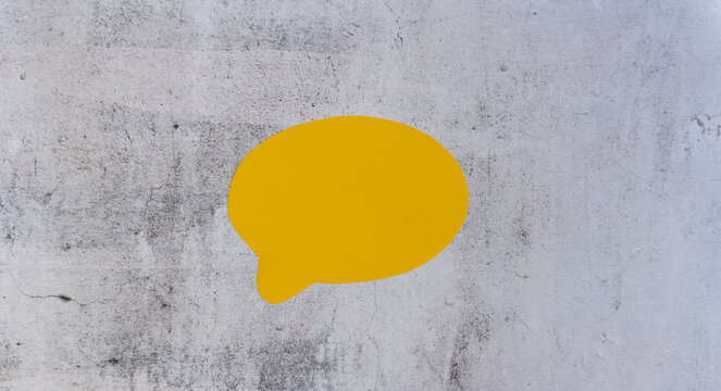 Single yellow speech bubble against rough gray concrete