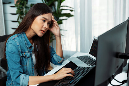 Young Asian IT developer analyzing online software development information on pc screens and laptop, creating program coding for latest version application on website with firmware updated. Stratagem.