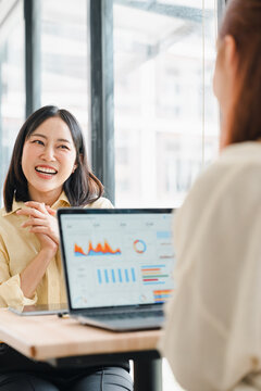Asian businesswoman smiling during a meeting with a colleague discussing data on a laptop screen