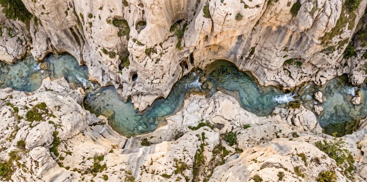 Aerial view of a winding turquoise river flowing through a deep limestone canyon with rugged rock formations, steep cliffs, and sparse green vegetation in a narrow mountain gorge