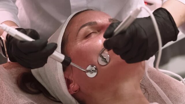 Microcurrent stimulation. Woman skin. Professional esthetician performing lifting facial procedure in gloves using modern device in salon.