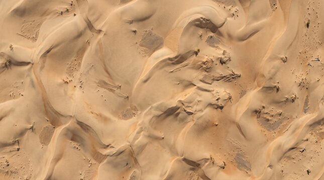 Aerial view of golden sand dunes in the desert, featuring undulating ridges, soft shadows, and wind-swept textures across a vast, arid landscape under bright sunlight