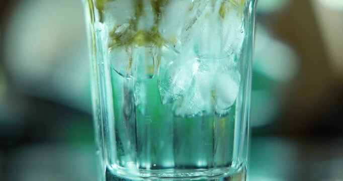 Macro close up pouring thick green matcha tea over ice cubes in a clear glass. Cinematic slow motion of refreshing cold summer beverage preparation. Iced green tea latte swirl background 4K video.