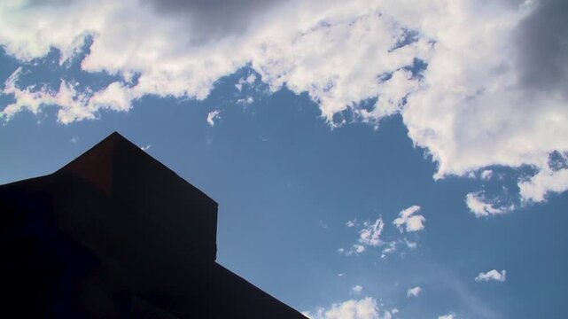 Slow motion silhouette of BMX rider doing backflip behind a blue sky with clouds