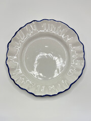 Top view of empty white ceramic plate with wavy blue rim on white background